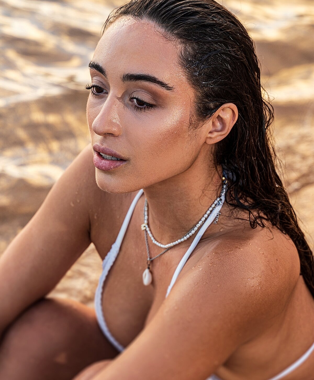 Woman with wet hair sitting on the beach.