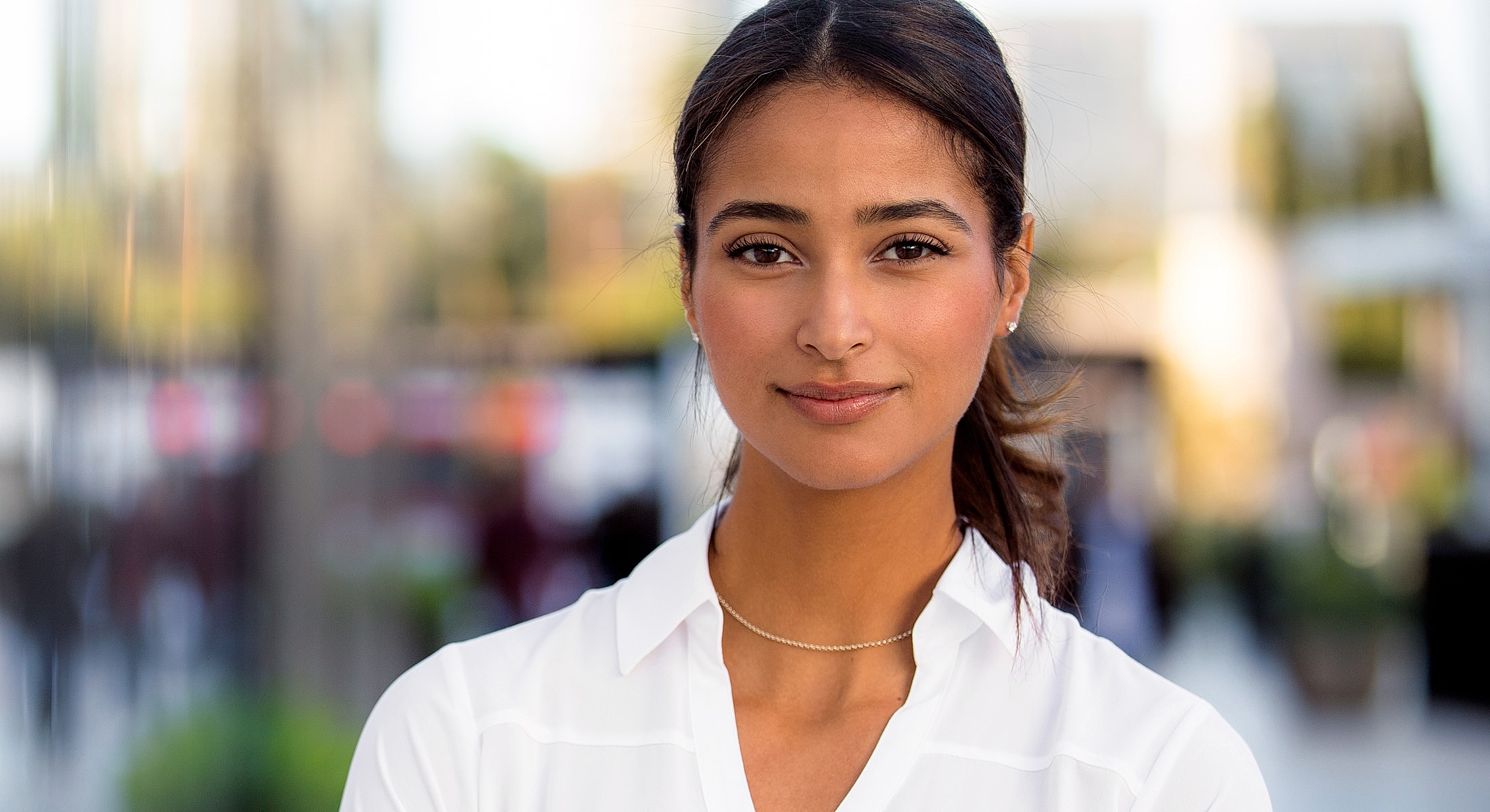 Woman smiling outdoors, wearing a white shirt.