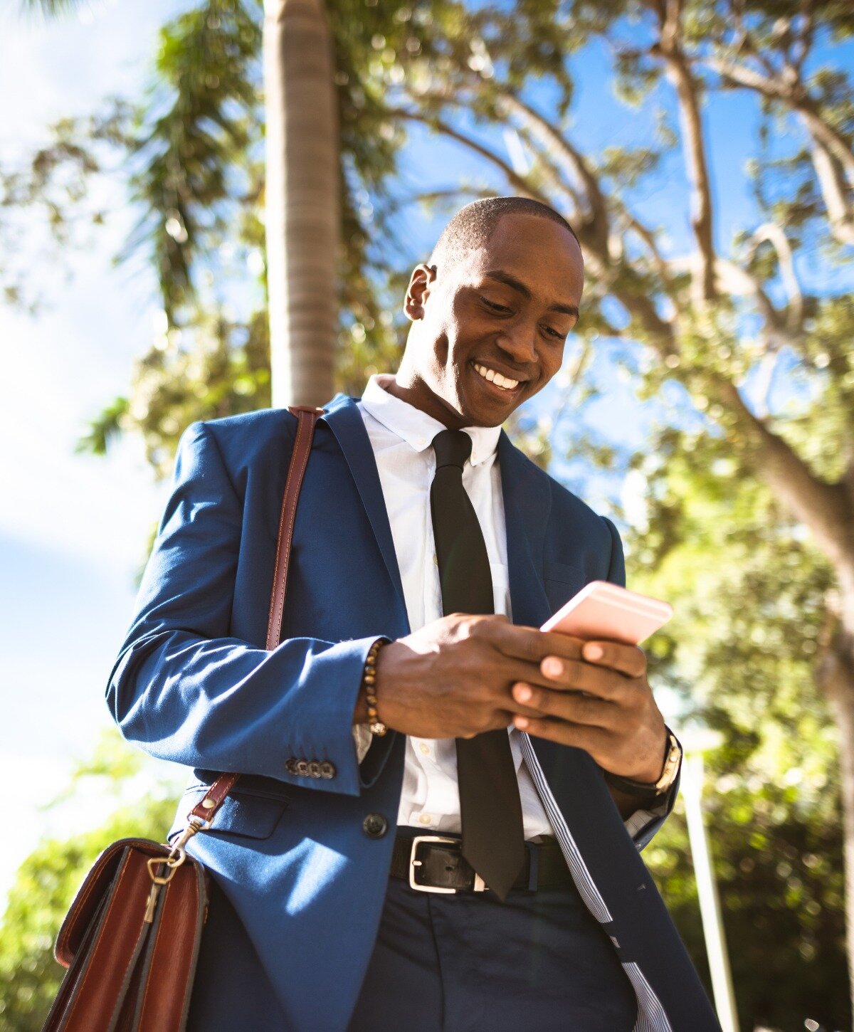 Business man smiling in a park while looking at his phone