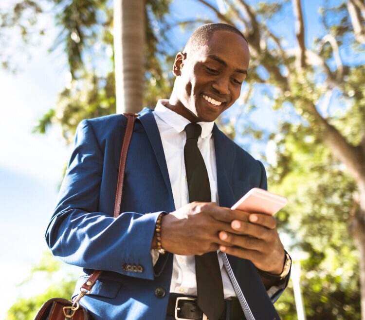 Wellness Feature - Business man smiling in a park while looking at his phone